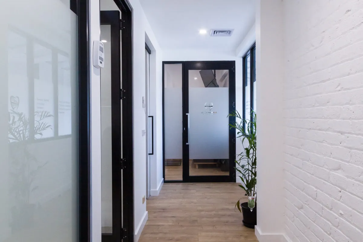 Internal corridor with timber floor, glass surgery doors, and an exposed painted-brick feature wall.