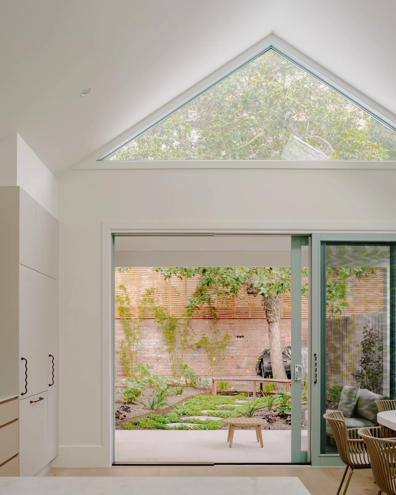 Kitchen view through sliding doors to the rear courtyard with a retained red-brick chimney and stepping-stone path through ground cover.
