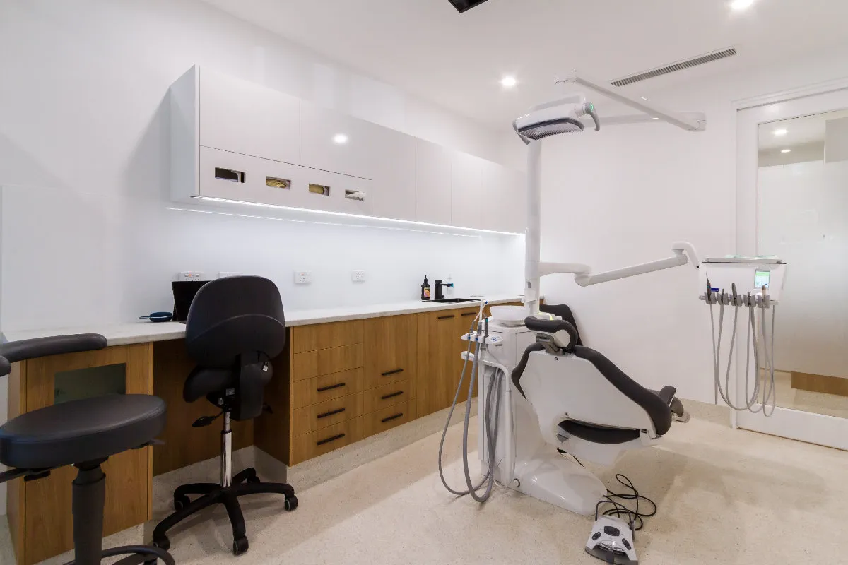 Second dental surgery room with chair, overhead light, and timber-and-white joinery.