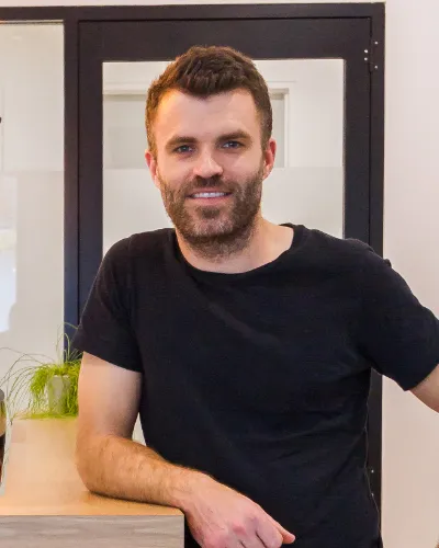 Founding director Dave Burmeister, smiling in a black t-shirt indoors.
