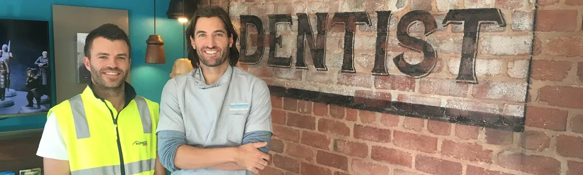A Burmpro builder beside Dr Dan Andrews in front of the heritage-painted DENTIST sign at Hobsons Bay Dental.